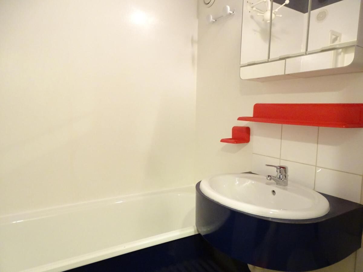 A bathroom with a white bathtub, a white sink with a red countertop, and a white mirror above the sink.