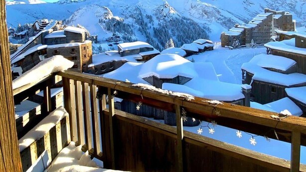 Un village de montagne enneigé, avec des bâtiments en bois et un ciel bleu azur.