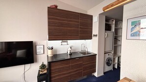 Une cuisine compacte équipée d’un lave-linge intégré, d’un téléviseur à écran plat et d’un tableau encadré au mur.