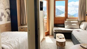 Habitación de hotel con dos camas, un sofá, una mesita y vistas a las montañas.