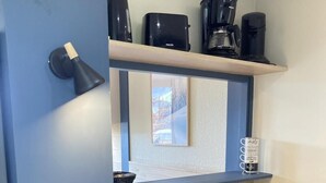 Una cocina moderna con un lavamanos de acero inoxidable, encimera de madera y cafeteras negras en un estante.