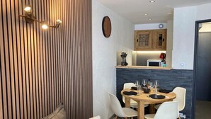 A modern living room with a dining area, wooden panel wall, and a kitchen in the background.