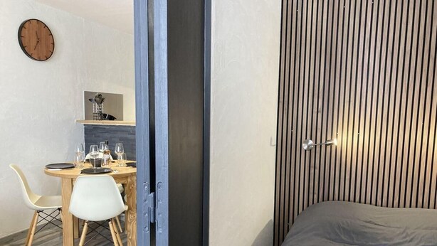 A modern room with a bed, a dining area with a table and chairs, and a vertical striped wall.
