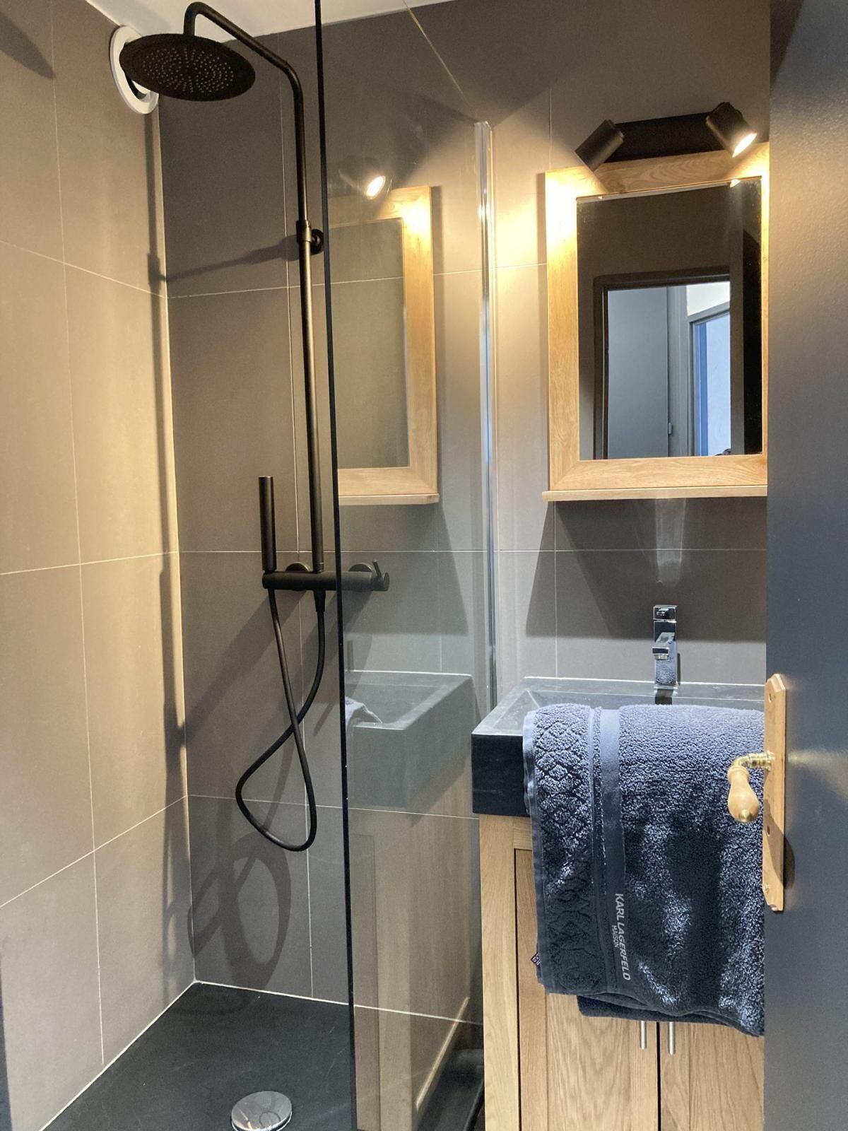 Ein modernes Badezimmer mit einer gläsernen Duschkabine, einem Holzlagerflansch und einem Spiegel über dem Waschbecken.