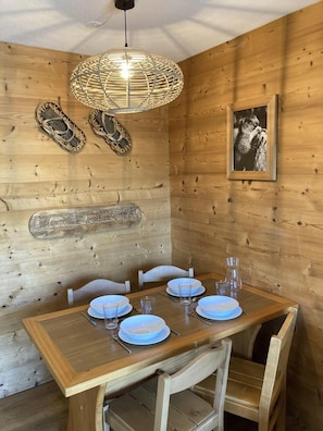 Interior de madeira com uma mesa de jantar posta para quatro pessoas, uma luminária de fibra natural e uma fotografia emoldurada na parede.