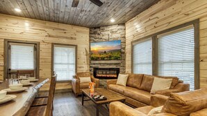 Ein gemütliches Blockhaus mit Holzwänden, einem Kamin aus Stein, Ledersofas und einem Essbereich mit einem langen Holztisch und Stühlen.
