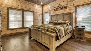 Ein Schlafzimmer mit Holzwänden, einem Bett, zwei Jalousienfenstern, einem Deckenventilator und einem Nachttisch mit Lampe.