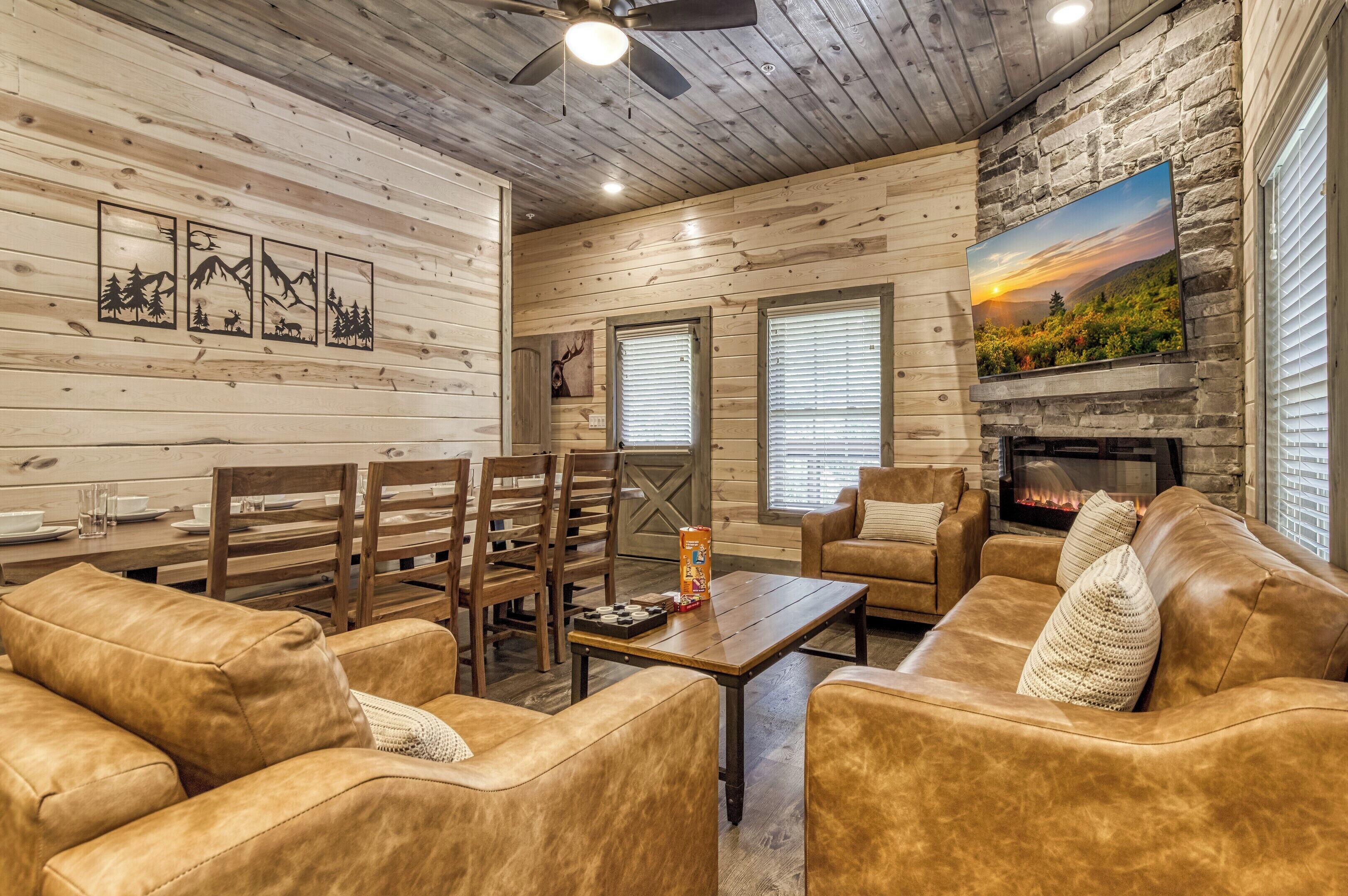 A cozy cabin interior with wooden walls, a fireplace, leather sofas, and a dining area.