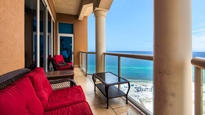 Un balcon avec des sièges rouges, une table en verre et une vue sur la plage.