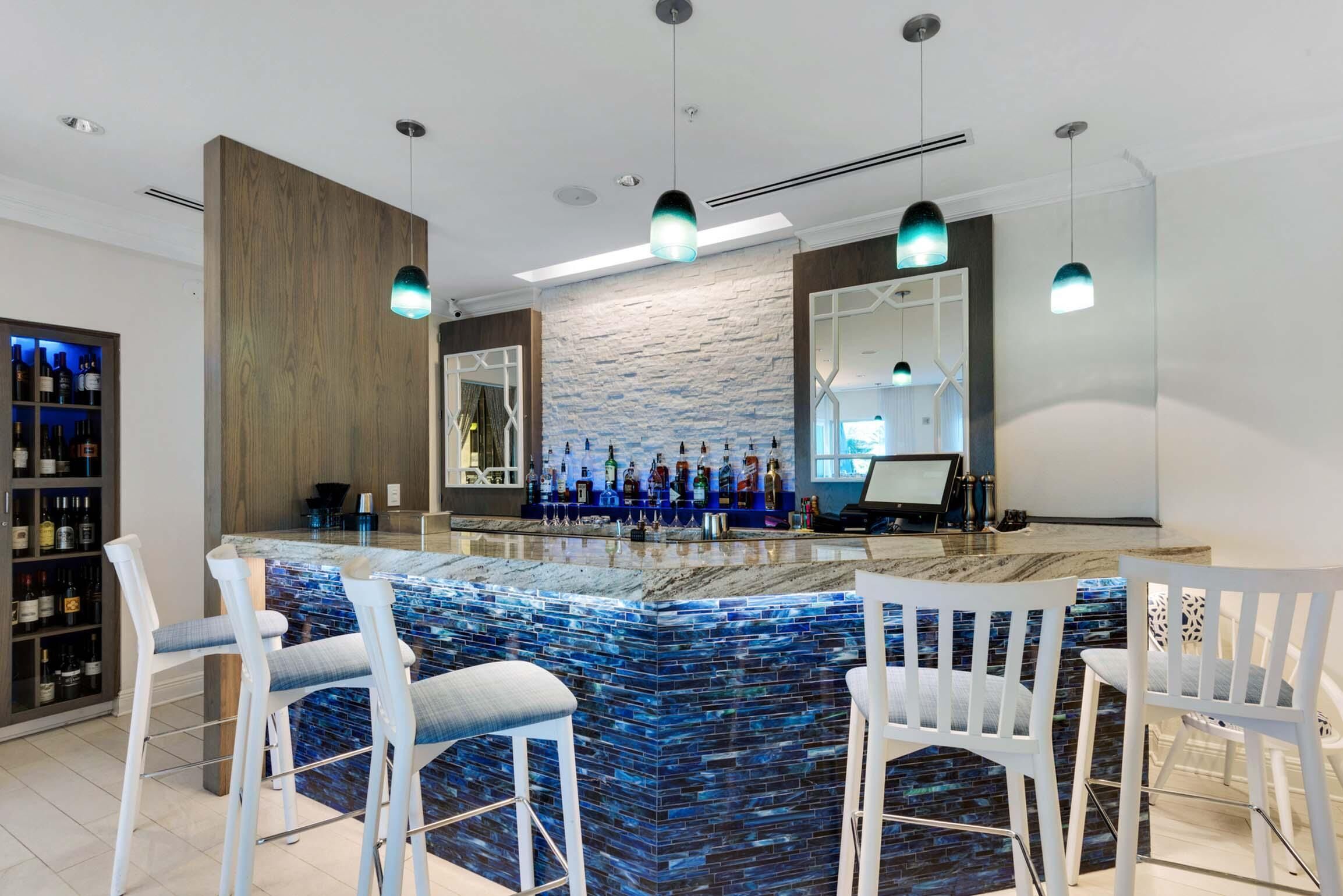 Un espacio de bar moderno con un respaldo de piedra, taburetes blancos y una vitrina para vinos.