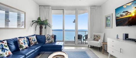 Una sala de estar con un sofá azul, un televisor y un balcón con vista al océano.