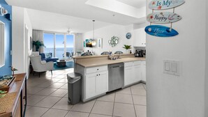 A modern kitchen with white cabinets, a dishwasher, and a countertop with a coffee maker. - Summerwind West 1203 (Navarre)