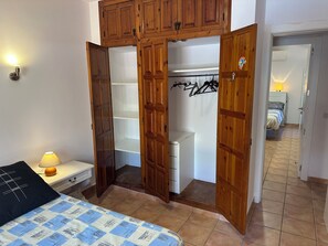 Ein Schlafzimmer mit einem Bett, einem Nachttisch, einem Holzschrank mit geöffneten Türen, die einen Kleiderschrank und ein Badezimmer zeigen, und einem Flur, der in einen anderen Raum führt.