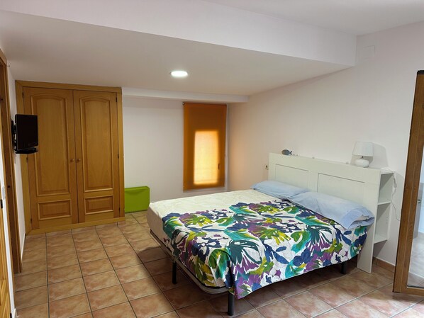 Ein Schlafzimmer mit Bett, Nachttisch, Fernseher, Fenster und Tür.