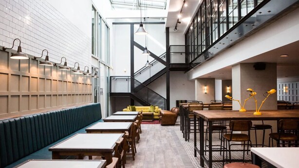 A modern interior with a long counter, seating area, and a staircase. - Chapter Kings Cross - Campus Accommodation (London)