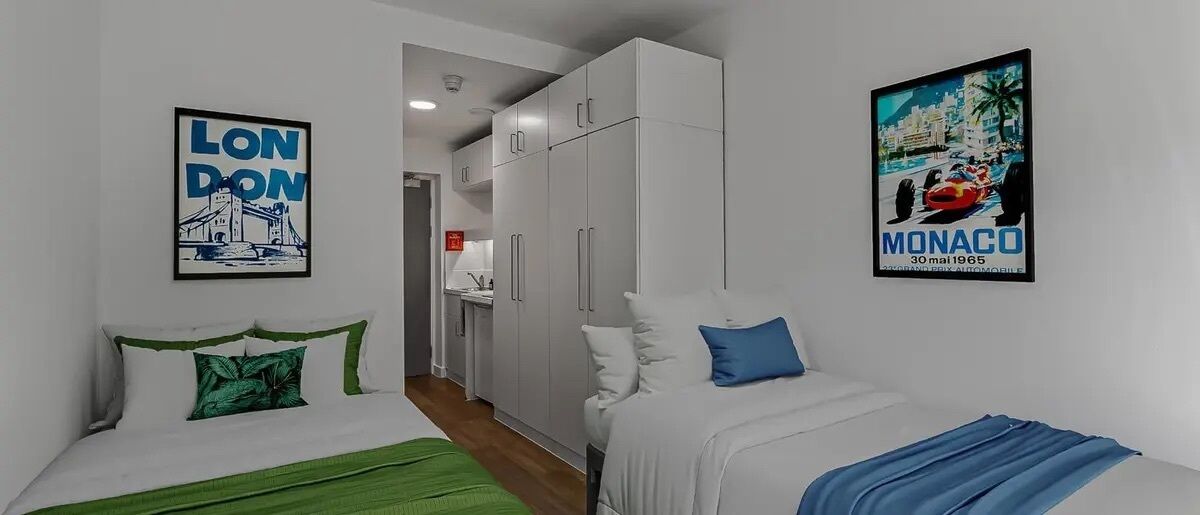 A bedroom with two beds, a wardrobe, and two posters on the walls.