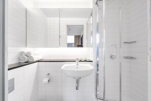 Een moderne badkamer met witte tegels, een wastafel, een douchecabine met glazen wanden en een handdoekrek met handdoeken.