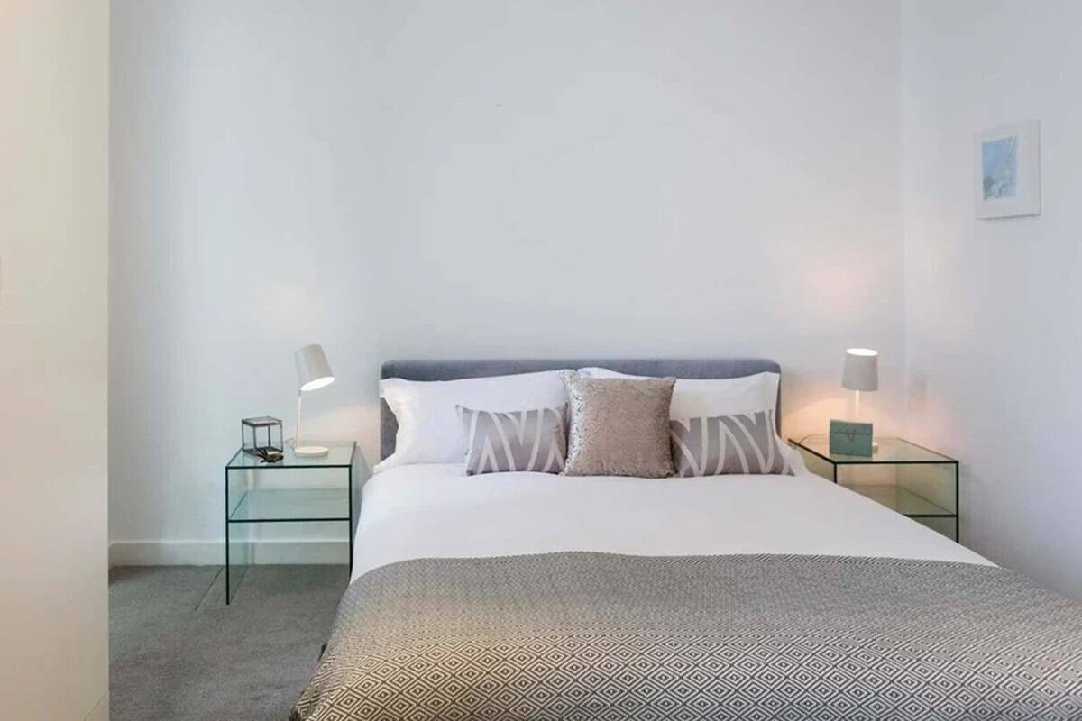 A minimalist bedroom with a large bed, two bedside tables with lamps, and a plain wall.