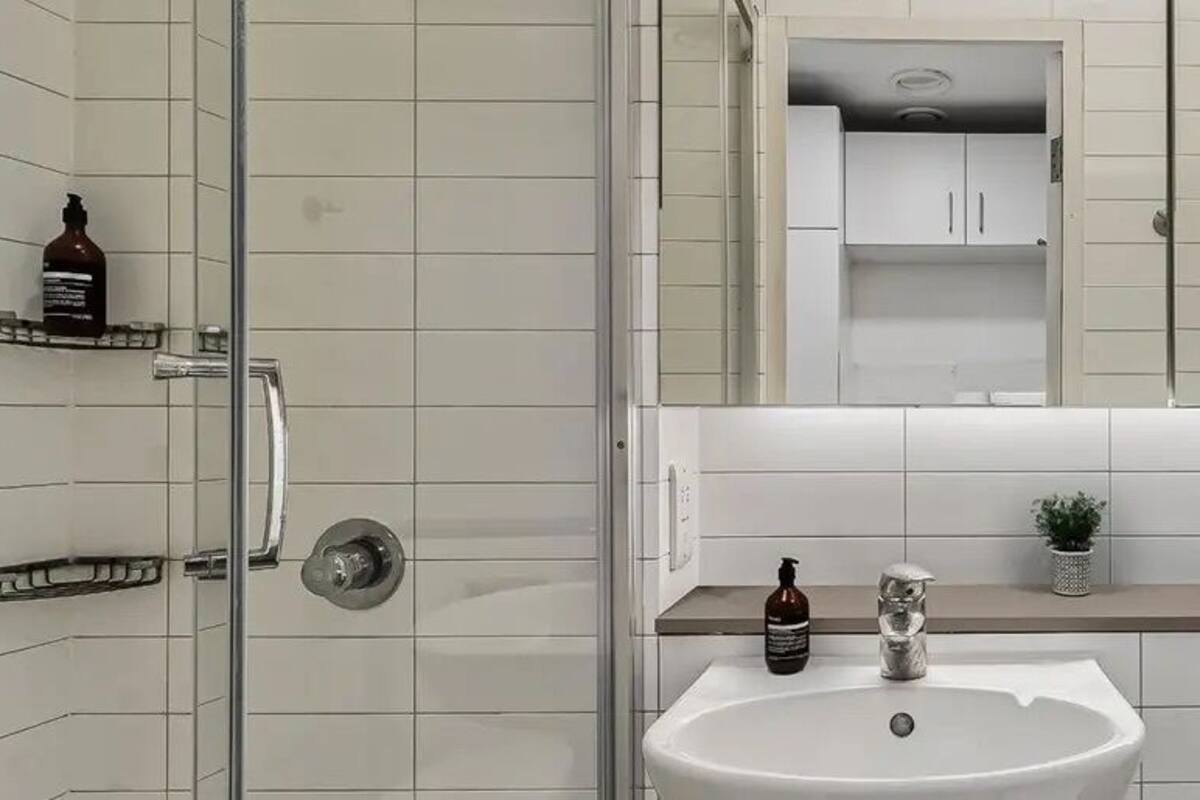 A modern bathroom with a glass shower enclosure, a white sink, and a countertop with toiletries.