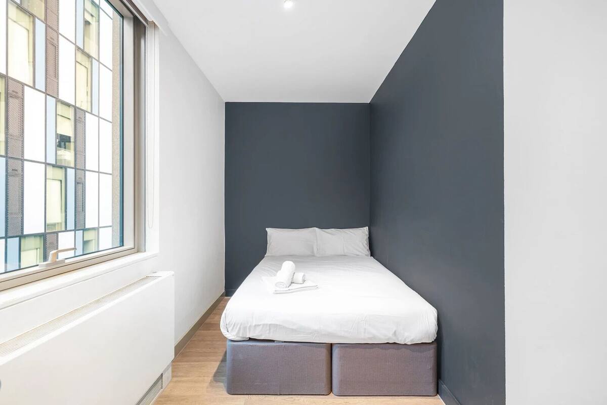 A narrow hotel room with a bed, a window, and a radiator.
