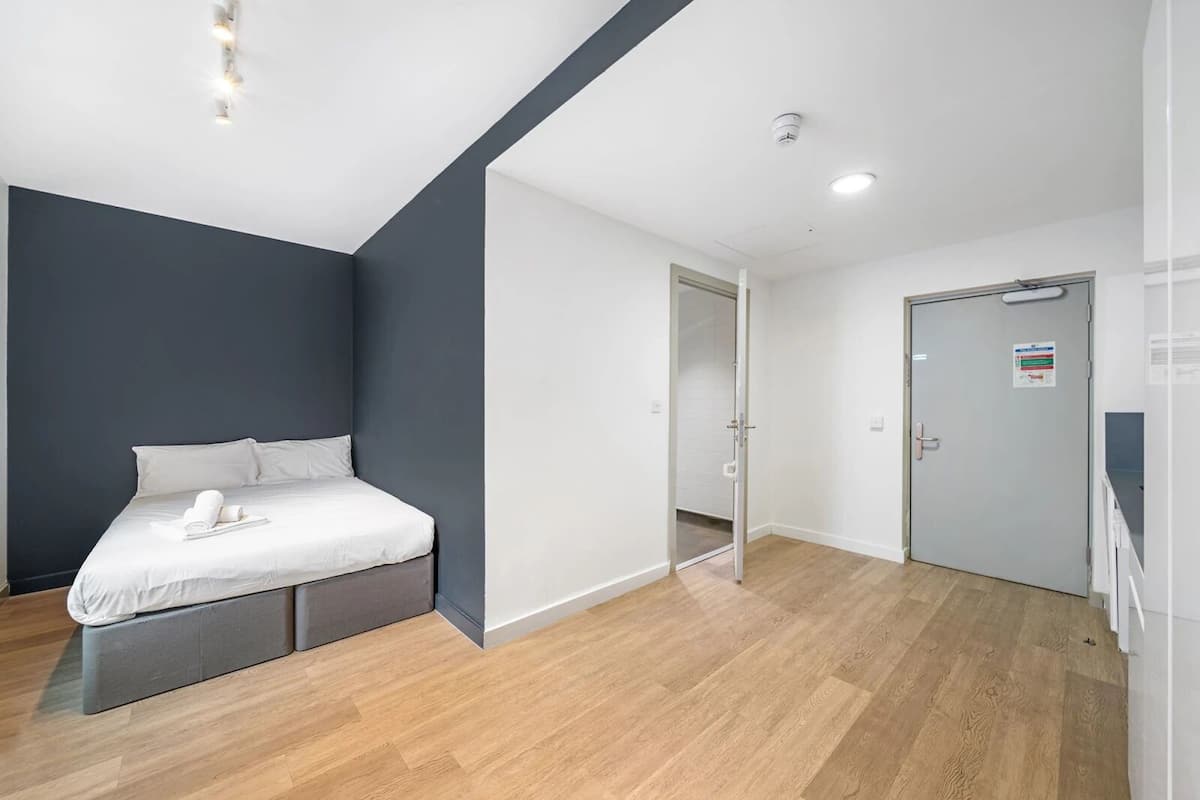 A modern bedroom with a bed, a wardrobe, and a door leading to another room.