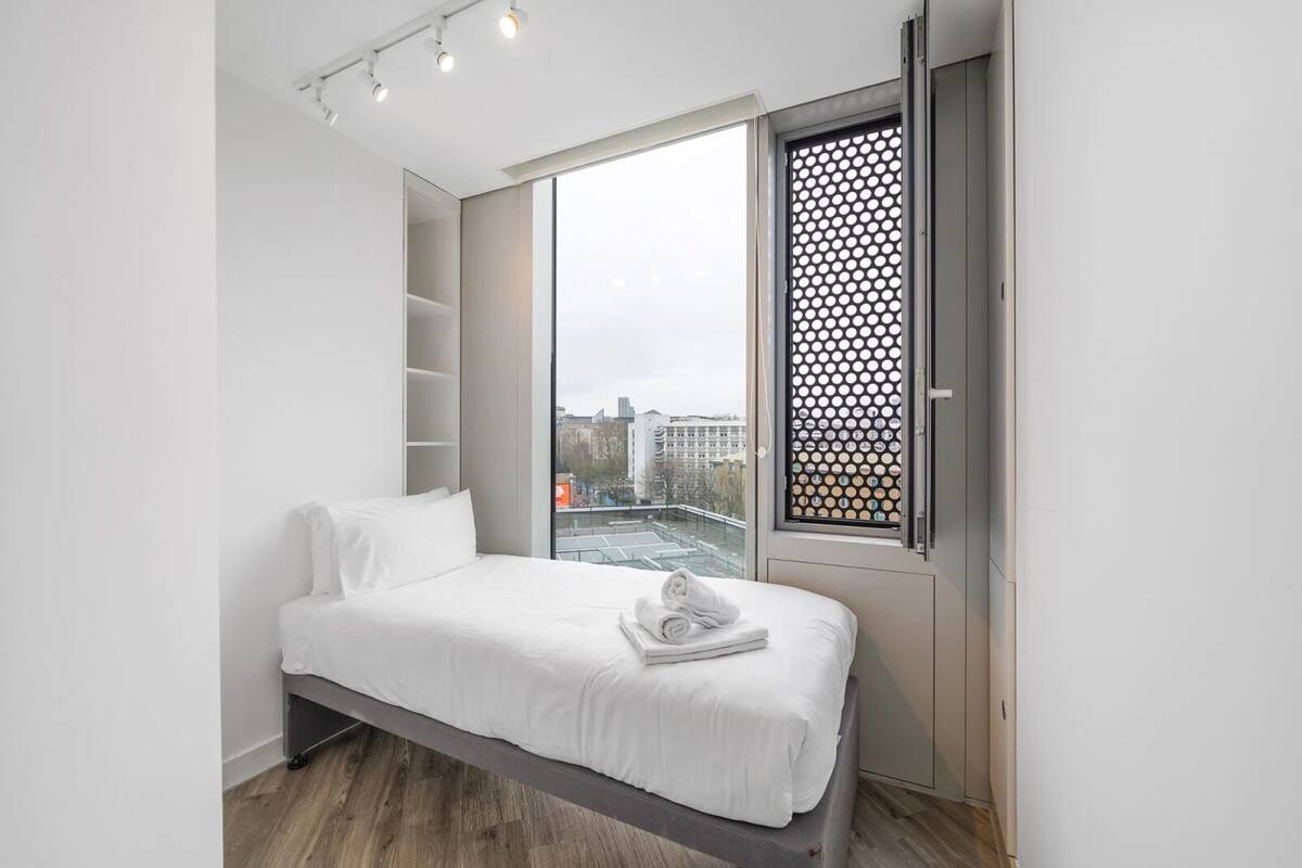 A modern bedroom with a bed, a large window, and a view of the city.