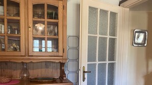 Ein Holzkabinett mit Glastüren, das Küchenutensilien beherbergt, eine Tür mit mattierten Glasfeldern sowie ein blauer Stuhl.
