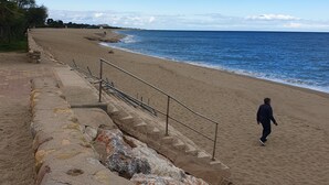 Ein Strand mit einer Steinmauer, einem Metallgeländer und einer Person, die darauf geht.