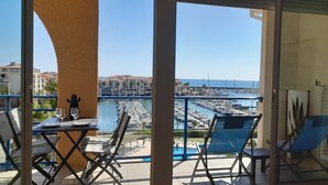Ein Balkon mit Blick auf einen Yachthafen und Gebäude. Liegestühle und ein Tisch mit Gläsern und einer Flasche sind vorhanden.