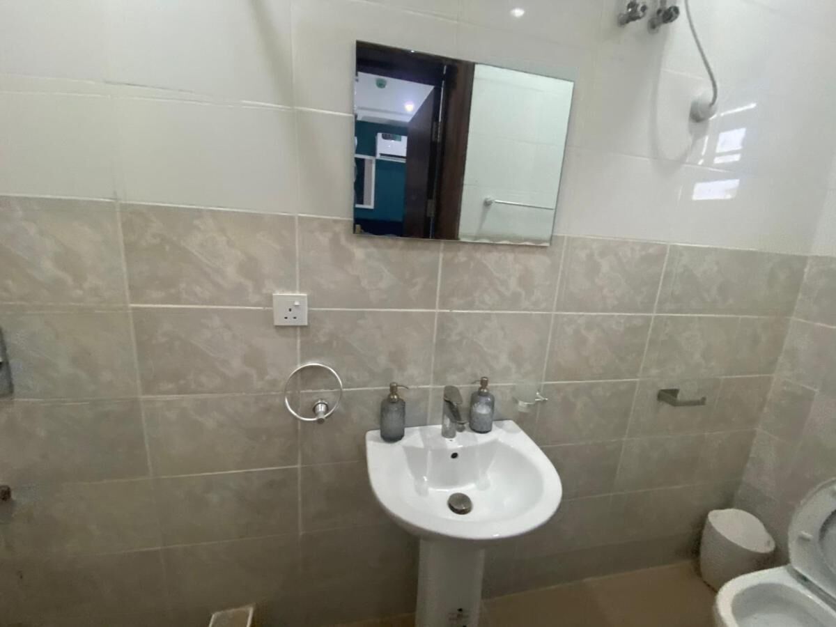 Un bagno con un lavandino bianco, due rubinetti, uno specchio sopra il lavandino e un water a destra.