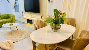 Un coin repas avec une table ronde, quatre chaises, une petite table d’appoint et un téléviseur en arrière-plan.