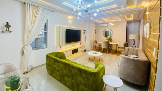 Un salon moderne avec un canapé vert, un téléviseur, un coin repas et une cuisine.
