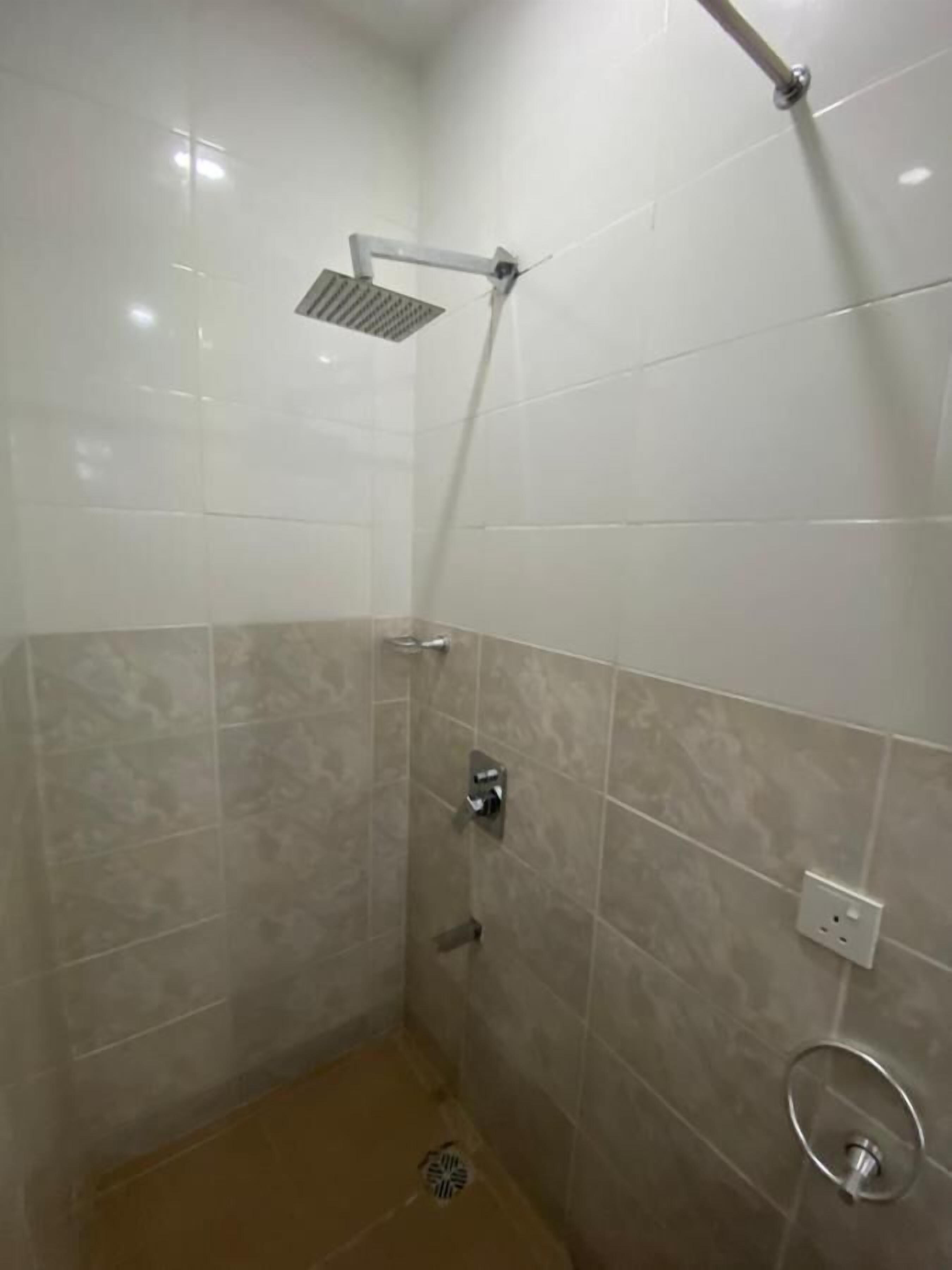 Ducha con cabezal de ducha de mano, panel de control en la pared y desagüe en el suelo.
