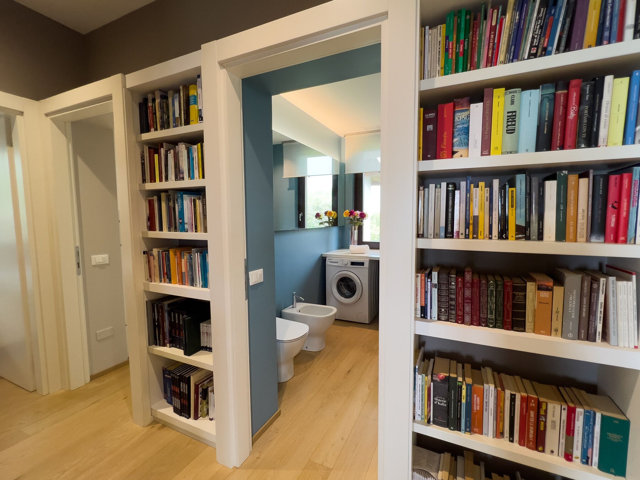 A hallway with bookshelves on both sides, leading to a bathroom with a washing machine and toilet.
