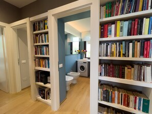 A hallway with bookshelves on both sides, leading to a bathroom with a washing machine and toilet.