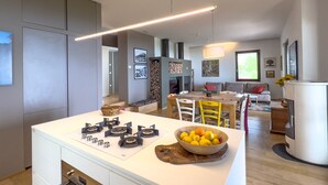 A modern kitchen with a central island, a dining area with a table and chairs, and a living space with a sofa and a fireplace.