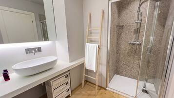 A modern bathroom with a large white sink, a glass shower enclosure, and a wooden ladder.