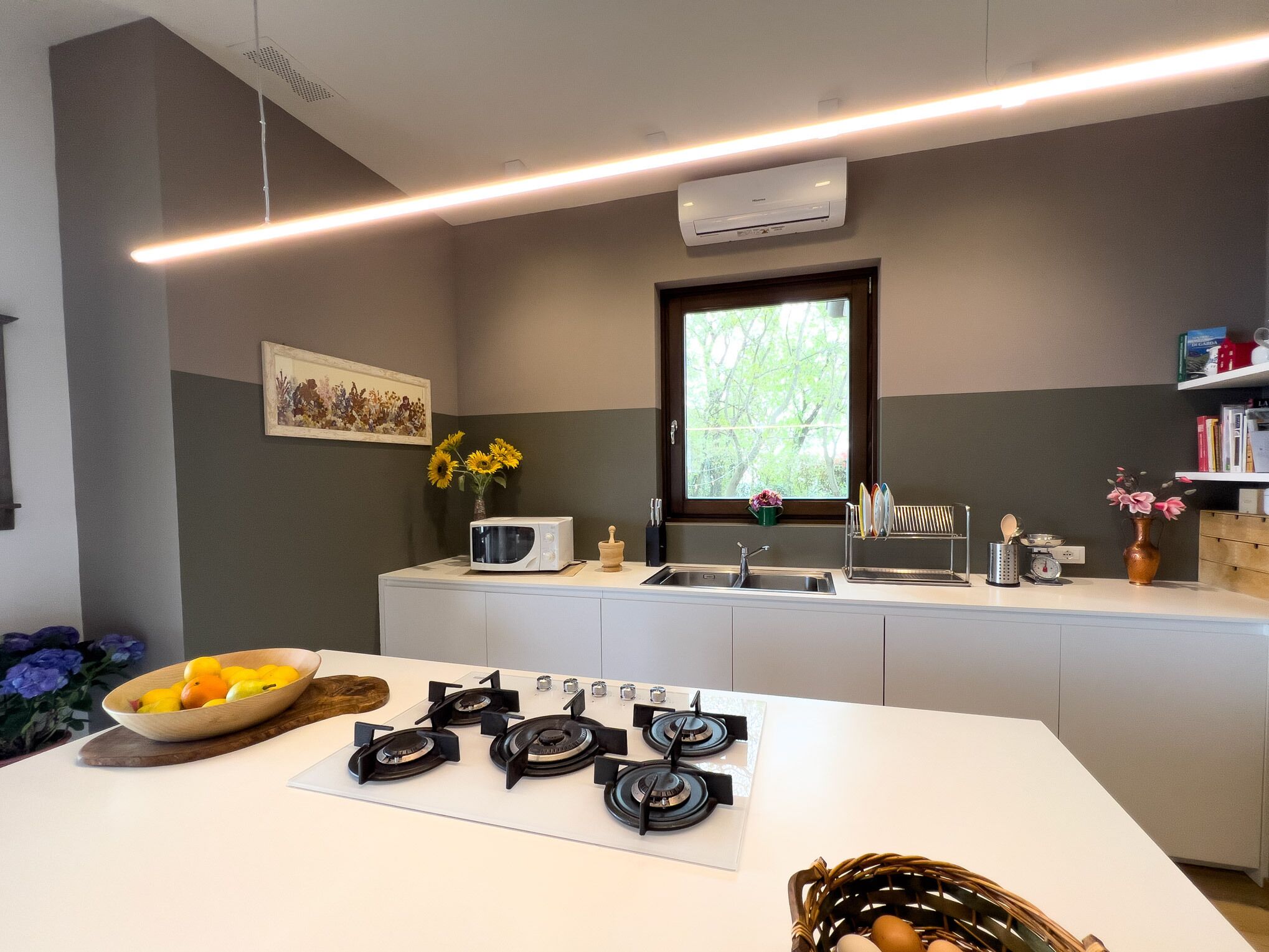 Una cucina moderna con un piano di lavoro bianco, un fornello integrato, un forno a microonde e una finestra vista alberi.