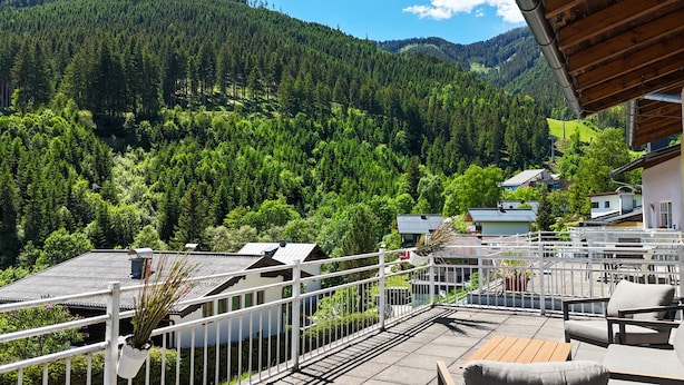 A terrace with outdoor seating, a view of a forested mountain, and a building with a sloped roof. - Penthouse Summer & Winter Fun 4, roof terrace (Zell am See)