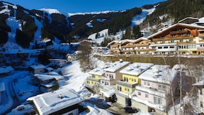 A snow-covered mountain village with traditional wooden buildings, a ski lift, and a clear blue sky. - Penthouse Summer & Winter Fun 4, roof terrace (Zell am See)