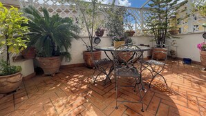 Un patio coperto con piastrelle in terracotta, piante in vaso e un tavolo in metallo con sedie.