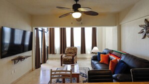 Una sala de estar con televisión de pantalla plana, ventilador de techo, sofá de cuero y un sillón estampado.