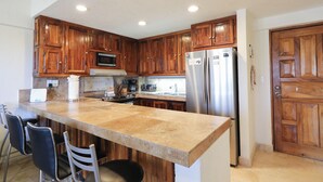 Una cocina con gabinetes de madera, un refrigerador de acero inoxidable, un microondas y una isla grande con taburetes de bar.