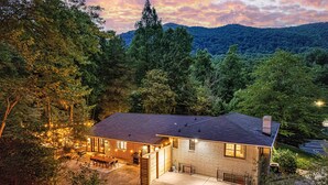 Una casa de dos plantas con un patio, rodeada de un bosque denso y colinas.