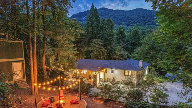 Una casa con un patio bien iluminado, rodeada de árboles y una montaña al fondo.