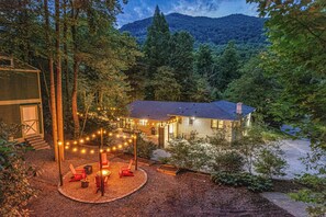 Une maison dotée d’un patio bien éclairé, entourée d’arbres et avec une montagne en toile de fond.