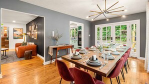 Un comedor moderno con una mesa de madera dispuesta para seis personas, sillas tapizadas en rojo y una lámpara de techo contemporánea.