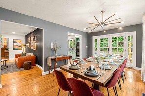 A modern dining area with a wooden table set for six, red upholstered chairs, and a contemporary chandelier. - 6BR Asheville House | Hot Tubs, Sauna + Theater (Fairview)