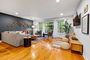 A modern living room with a grey sofa, wooden coffee table, and a wooden console table with decorative items. - 6BR Asheville House | Hot Tubs, Sauna + Theater (Fairview)