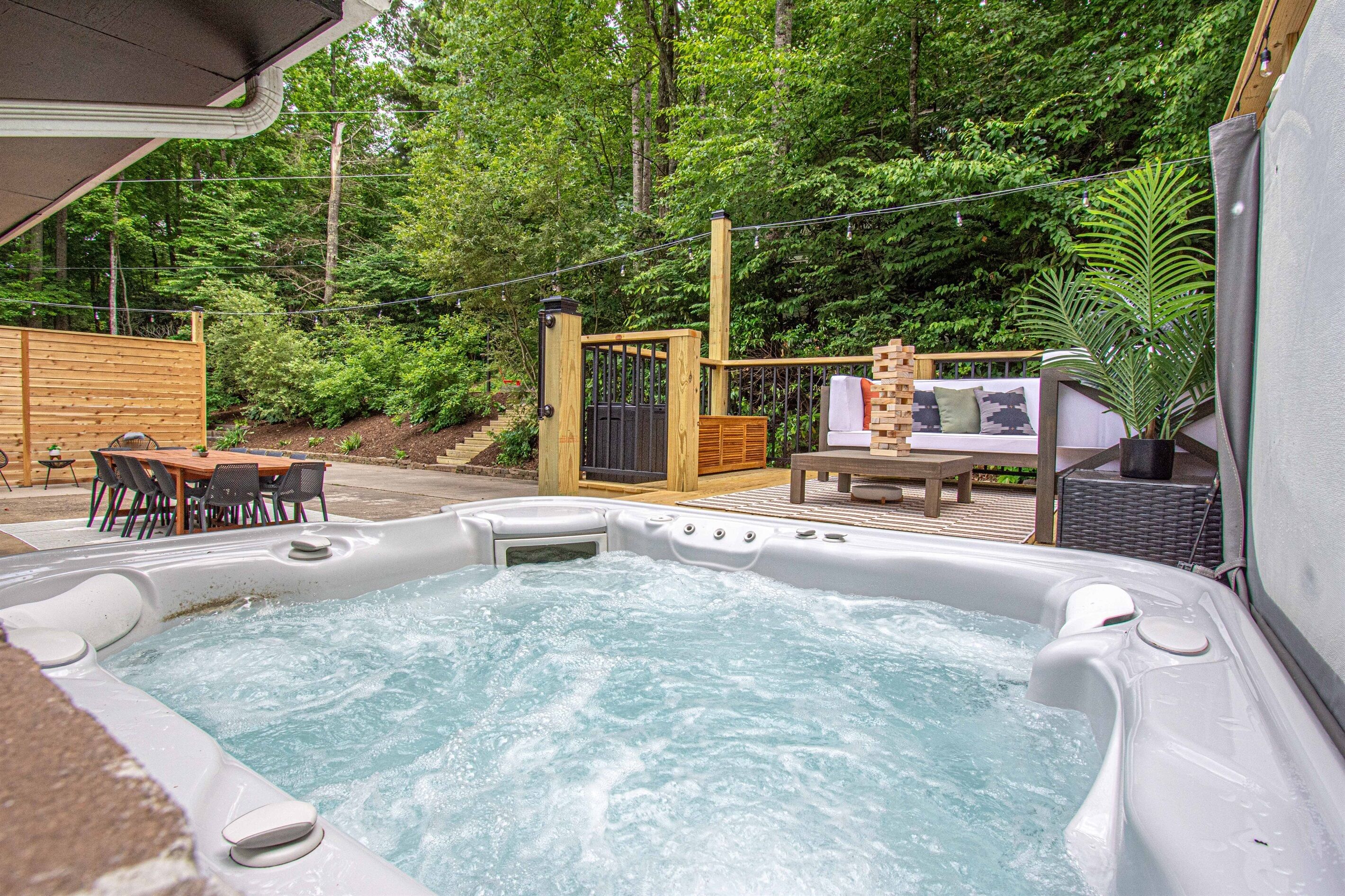 Un bain à remous doté d’une terrasse en bois, entouré d’une végétation luxuriante et d’une clôture en bois.